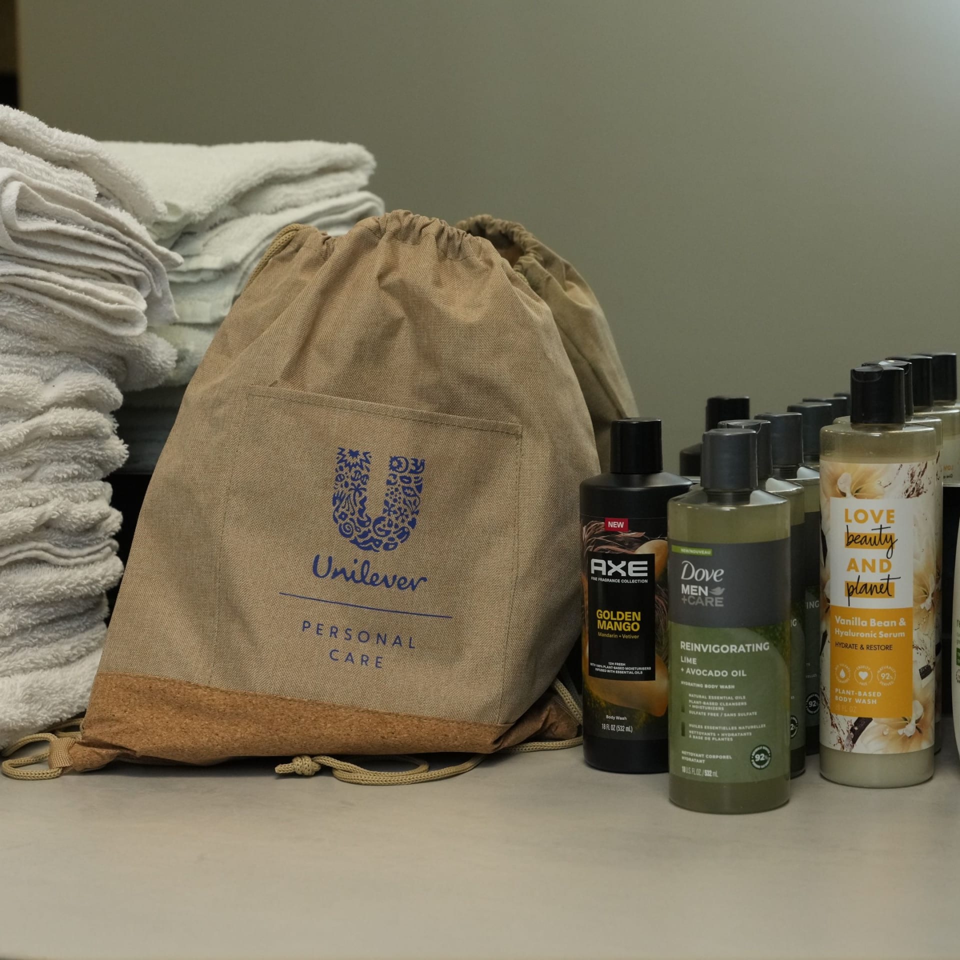image: Unilever Personal Care branded drawstring bag displayed with Dove, Axe, and Love Beauty and Love Beauty and Planet shower products beside stacked white towels.